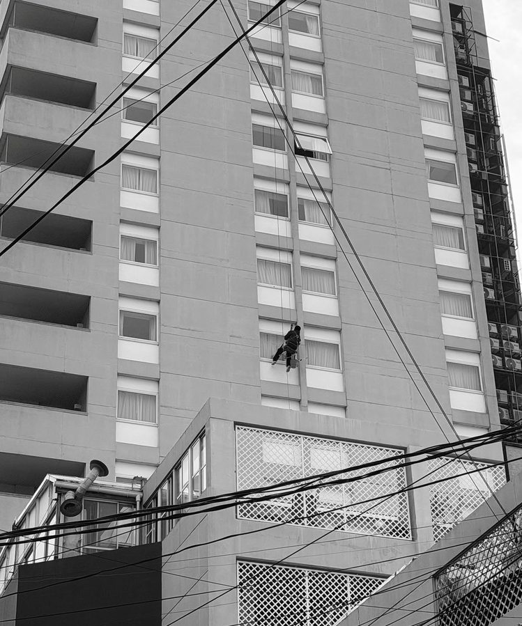 Operario con arnés limpiando vidrios en altura en la fachada de un edificio
